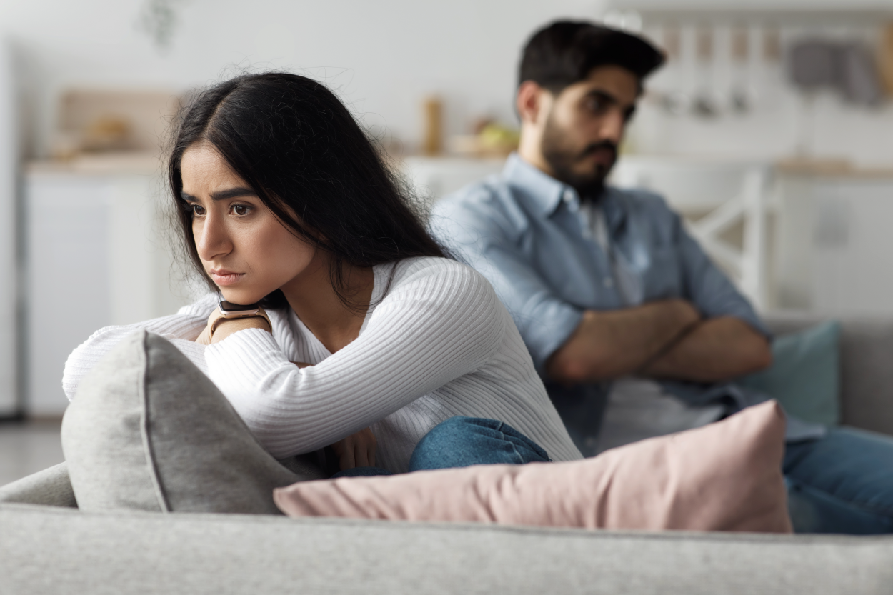 Two people sitting facing away from each other with upset looks on their face