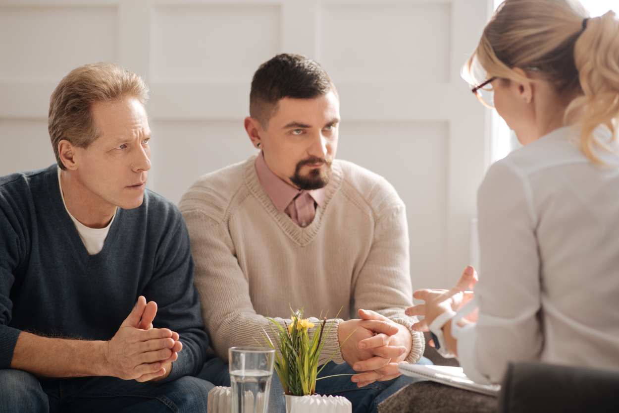 Two men sit side by side across from a woman