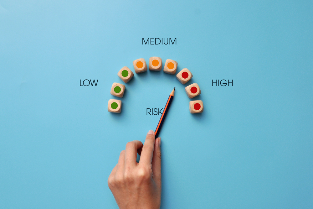 Wooden cubes in the form of a speedometer showing the risk assessment. Hand holding pencil is pointing toward medium to high risk.