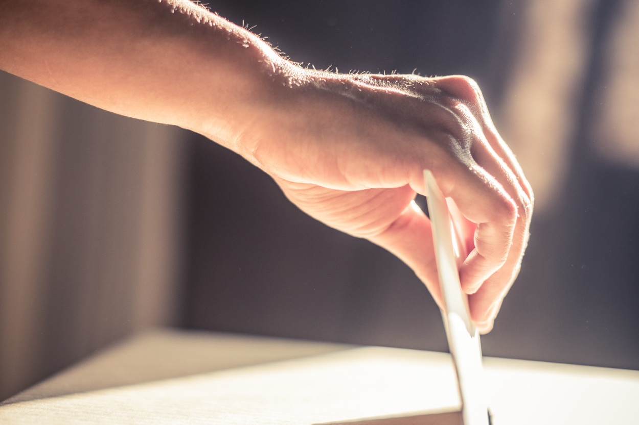 close up of a hand inserting a ballot into the ballot box