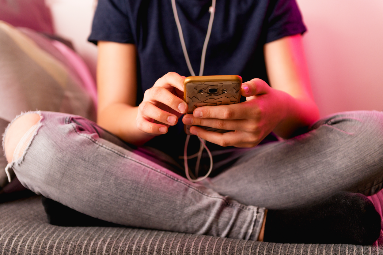 close up of a teenager on their phone; legs crossed; phone in hands